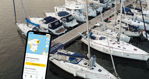 Ein Smartphone mit der ADAC Skipper App vor dem Hintergrund einer Marina in Italien.